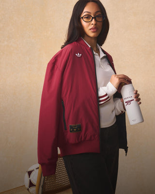 Stanley 1913 white water bottle held by a woman wearing a red Arsenal x Adidas bomber jacket