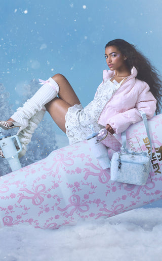 Stanley 1913 tumbler and cooler bag in soft blue and pink bow print, styled with a model on a snowy sled scene.