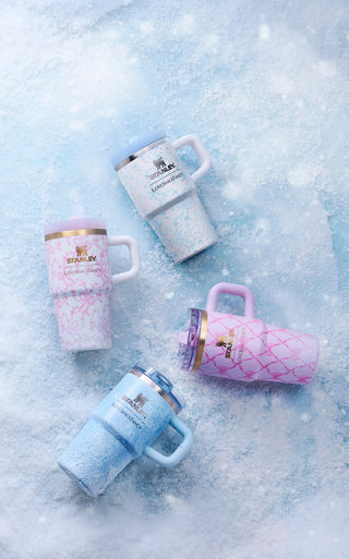 Four Stanley 1913 x LoveShackFancy tumblers in pink, blue, and white floral and bow patterns, resting on icy snow.