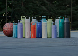 Stanley 1913 water bottles in multiple colors lined up on a basketball court beside a basketball.